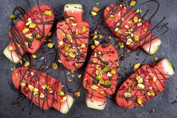 Slices watermelon in ice cream or popsicle shape with chocolate and pistachio nuts decoration on slate board, flat lay