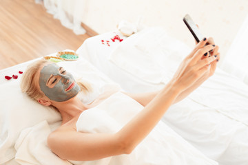 Obraz na płótnie Canvas Shot of relax beautiful middle-aged woman selfie or video call to her friend while having a clay mask treatment at spa salon, concept woman leisure time, spa treatment, beauty and healthcare lifestyle