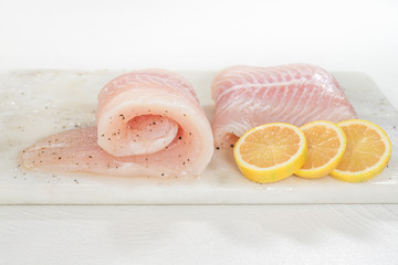 Fresh raw fish fillet. Fillet of sea bass and slices of pink lemon close up on a marble cutting board on white background, front view