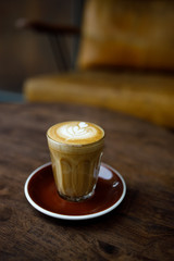 small cup of coffee with heart pattern froth on wooden table