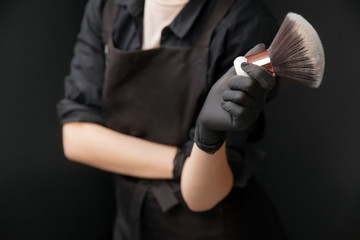 Master make-up artist holds brush for white powder with dust on black background for tan spray skin