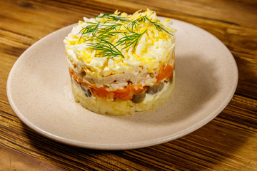 Tasty layered salad with potatoes, chicken breast, marinated mushrooms, carrots, eggs and mayonnaise on wooden table