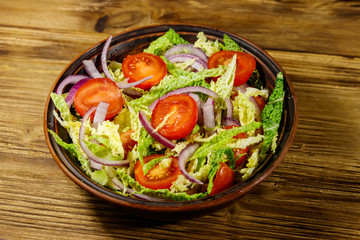 Healthy salad with savoy cabbage, cherry tomato, red onion and olive oil on wooden table