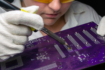 Woman master solders a motherboard with a soldering iron