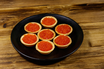 Tartlets with red caviar on a wooden table
