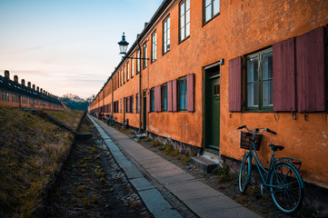 Fototapeta na wymiar Bicycle leaned on the wall of grating old red and orange brick residential building. The narrow industrial streets on Copenhagen in Denmark. Focused on bike, traditional ecology transportation way