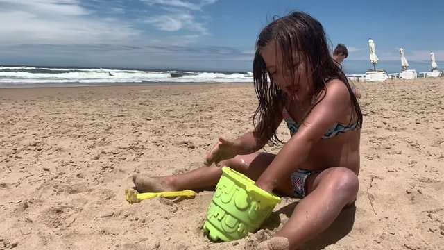 Little girl child playing with sand and bucket at beach shore