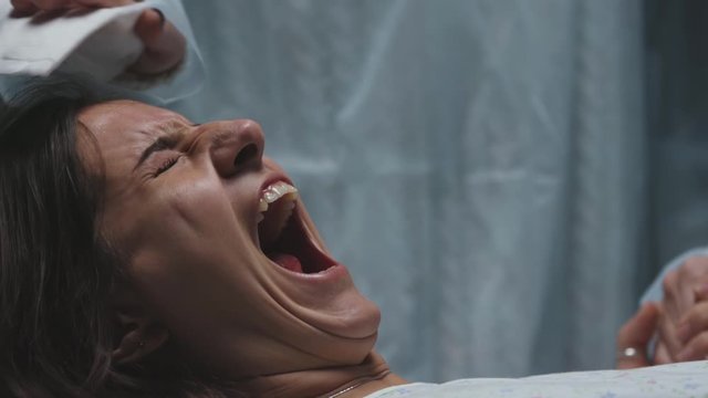 woman in labor in maternity ward gives birth to child pushing haard and scream and shout, portrait of young Caucasian pregnant mother waiting for baby and feeling severe pain
