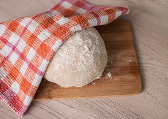 Round piece of dough on a wooden cutting board