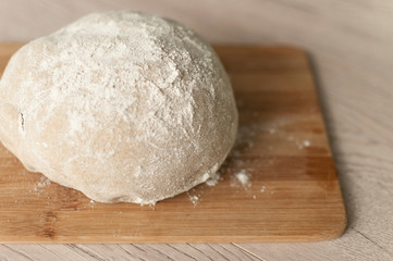 Round piece of dough on a wooden cutting board