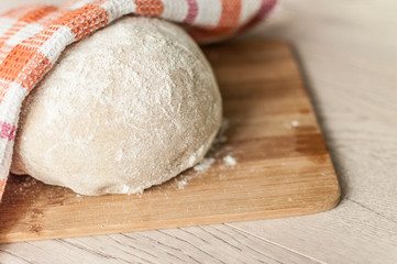 Round piece of dough on a wooden cutting board