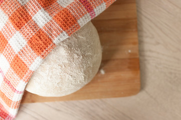 Round piece of dough on a wooden cutting board