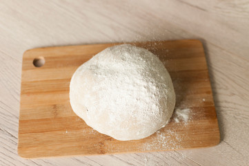 Round piece of dough on a wooden cutting board