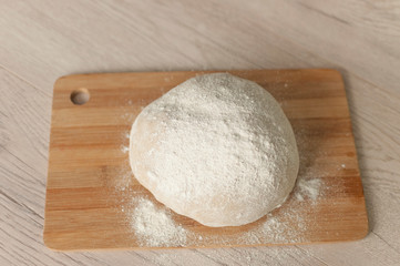 Round piece of dough on a wooden cutting board