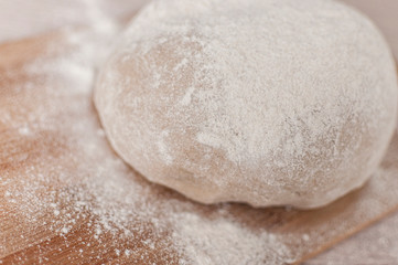 Round piece of dough on a wooden cutting board