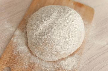 Round piece of dough on a wooden cutting board