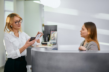 friendly administrator and beautiful caucasian client in beauty saloon, look at each other and smile, friendly staff in beauty saloon. Young woman came to get beauty procedures