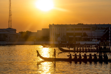 Silhouette of people rowing a long boat to celebrate Thailand boat traditional ceremony with sun flare and sunset background on Chao Phaya river, bangkok, Thailand 