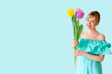 Portrait of a beautiful young girl in a dress holding a bouquet of large tulips posing on a turquoise background. Women's day, holiday, surrealism