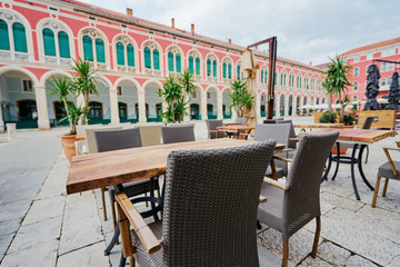 Sidewalk cafe near ancient bulding with green wooden windows.