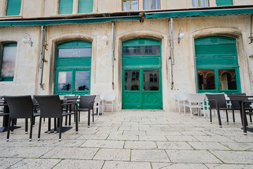 Sidewalk cafe near ancient bulding with green wooden windows.