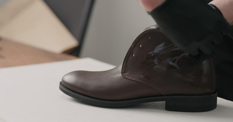 man hands in black gloves applying protective cream to brown leather chukka boots