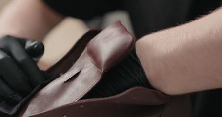 man hands in black gloves applying protective cream to brown leather sneakers