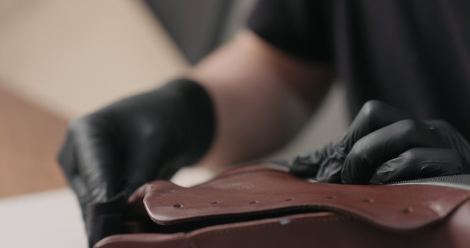 man hands in black gloves applying protective cream to brown leather sneakers