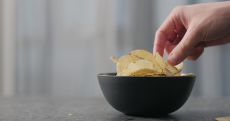 man hand take potato chip with plack pepper from black bowl on concrtete countertop