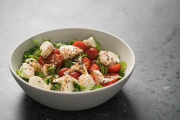 Salad with cherry tomatoes, mozzarella and frisee leaves in white bowl on concrete background
