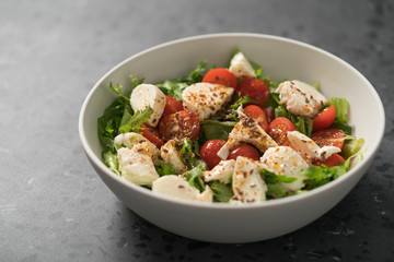 Salad with cherry tomatoes, mozzarella and frisee leaves in white bowl on concrete background