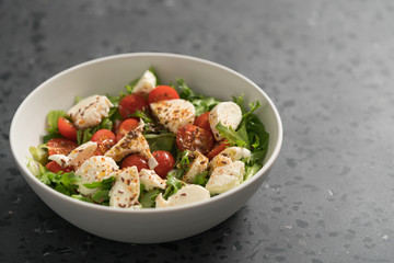Salad with cherry tomatoes, mozzarella and frisee leaves in white bowl on concrete background