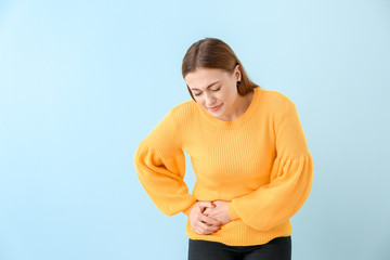 Young woman suffering from abdominal pain on color background
