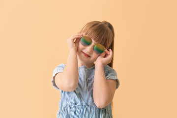 Funny little girl with sunglasses on color background