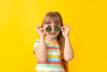 Funny little girl with sunglasses on color background