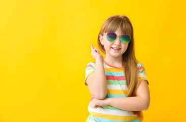 Funny little girl with sunglasses on color background