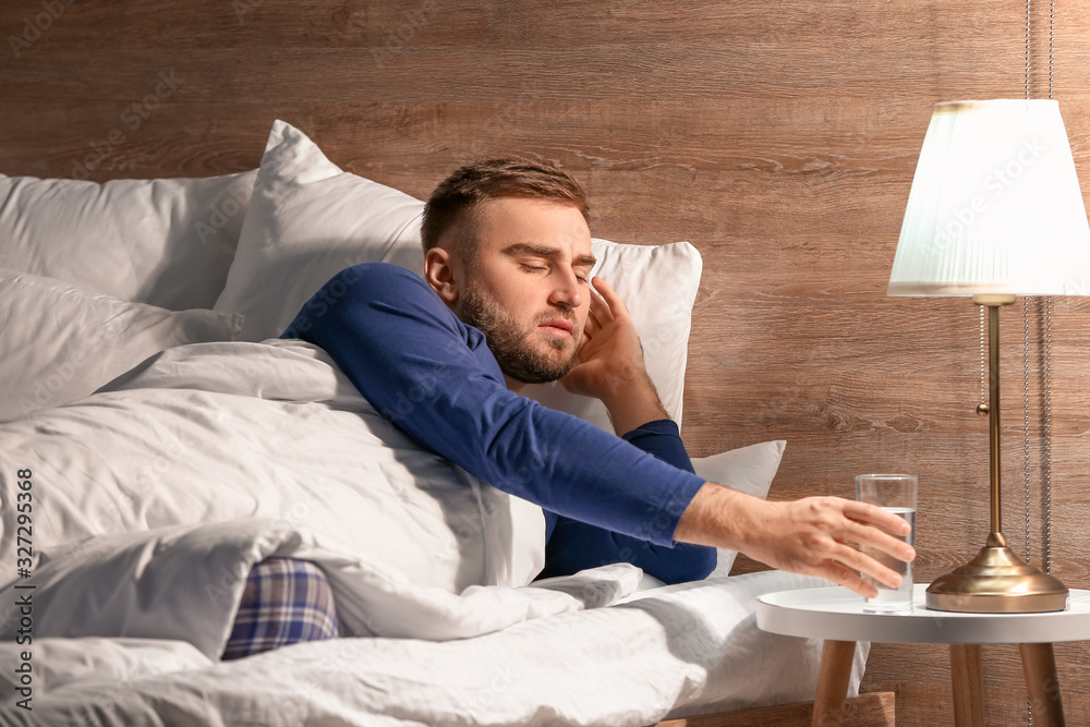 Wall mural young man taking glass of water from bedside table at night