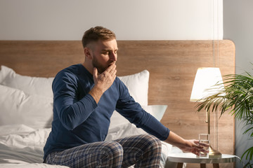 Young man taking glass of water from bedside table at night