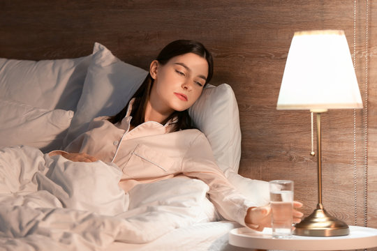 Beautiful Young Woman Taking Glass Of Water From Bedside Table In Evening