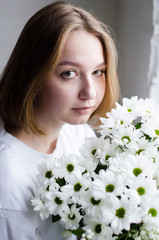 portrait of a young beautiful girl with blond hair and a short haircut with white flowers in her hands on a white background, the concept of beauty and health