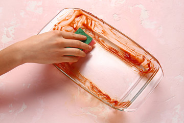 Woman washing dirty baking dish on color background