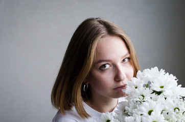portrait of a young beautiful girl with blond hair and a short haircut with white flowers in her hands on a white background, the concept of beauty and health