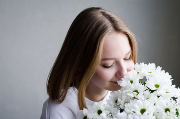 portrait of a young beautiful girl with blond hair and a short haircut with white flowers in her hands on a white background, the concept of beauty and health