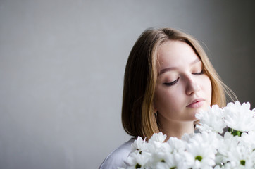 portrait of a young beautiful girl with blond hair and a short haircut with white flowers in her hands on a white background, the concept of beauty and health