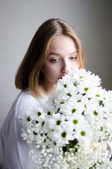 portrait of a young beautiful girl with blond hair and a short haircut with white flowers in her hands on a white background, the concept of beauty and health