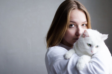portrait of a young beautiful girl in a white sweater on a white background with a cute white cat in her arms. Kitten enjoys being in girls arms.