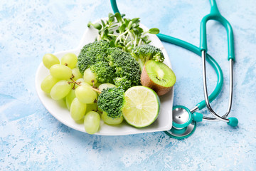 Plate with healthy products and stethoscope on color background