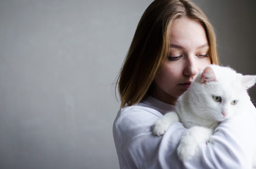 portrait of a young beautiful girl in a white sweater on a white background with a cute white cat in her arms. Kitten enjoys being in girls arms.