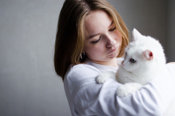 portrait of a young beautiful girl in a white sweater on a white background with a cute white cat in her arms. Kitten enjoys being in girls arms.