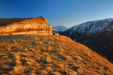 The tent stands on the edge of a cliff under a beautiful rock, good sunset light, a beautiful landscape.